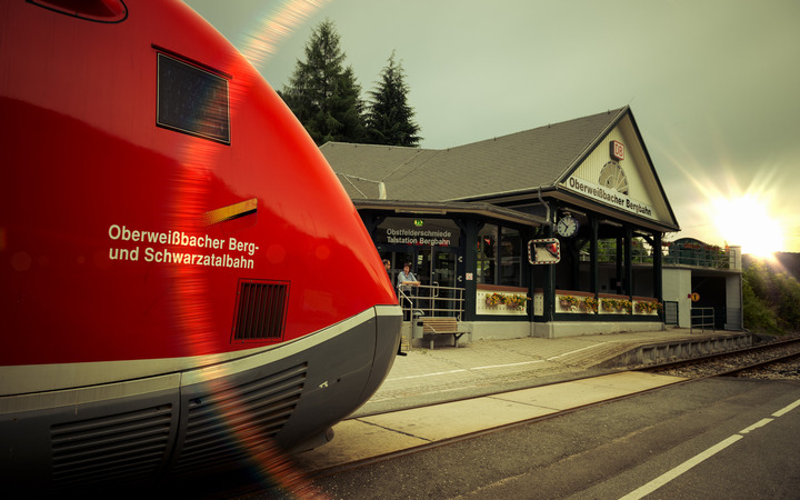 Ein Zug der Schwarzatalbahn steht vor dem Bahnhof Obstfelderschmiede in der Abendsonne.