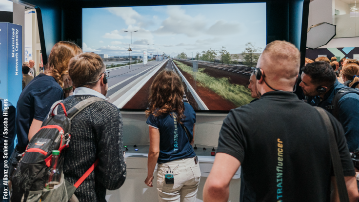 Die Trainfluencer blicken auf einen Zugsimulator bei der InnoTrans.